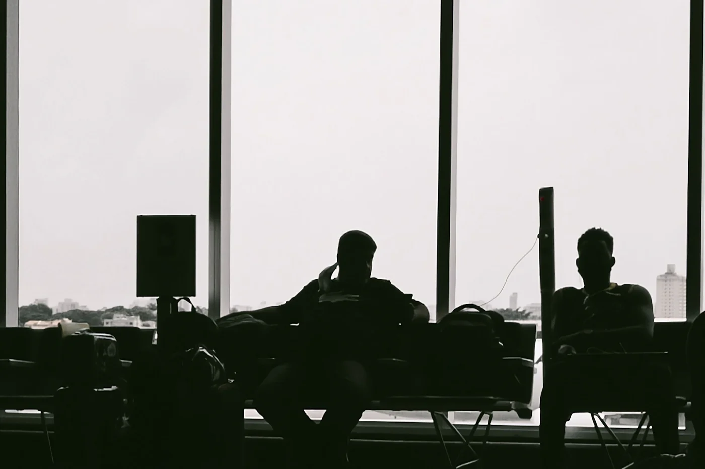 Two travellers waiting in silhouette against the windows of an airport terminal