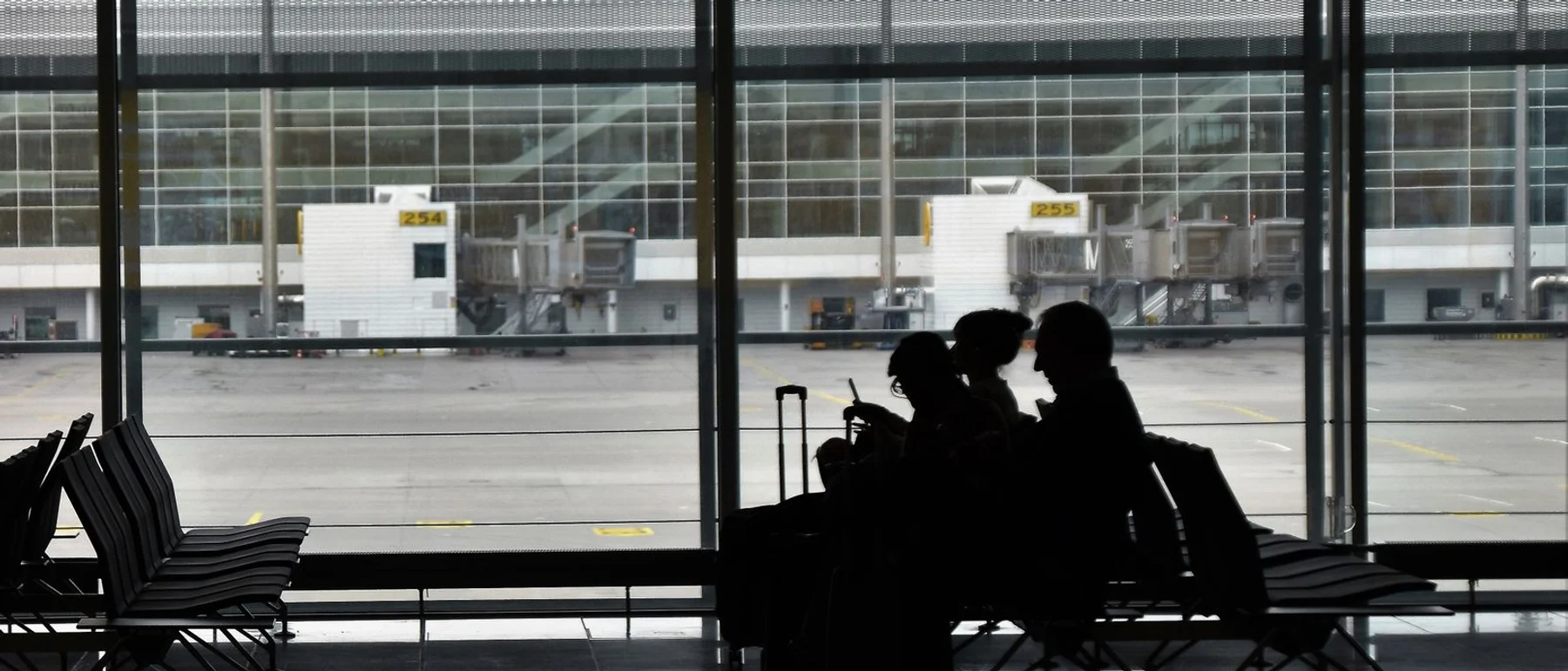 Travellers waiting with luggage in silhouette at an airport departure gate